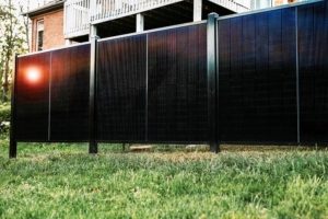 modern solar panel fence beside a brick house under a clear blue sky with sunlight reflecting off the panels