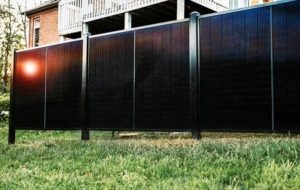 modern solar panel fence beside a brick house under a clear blue sky with sunlight reflecting off the panels